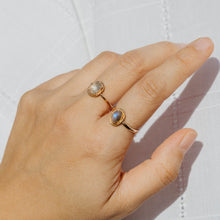 Load image into Gallery viewer, Hand wearing a gold ring with a labradorite stone on a white background
